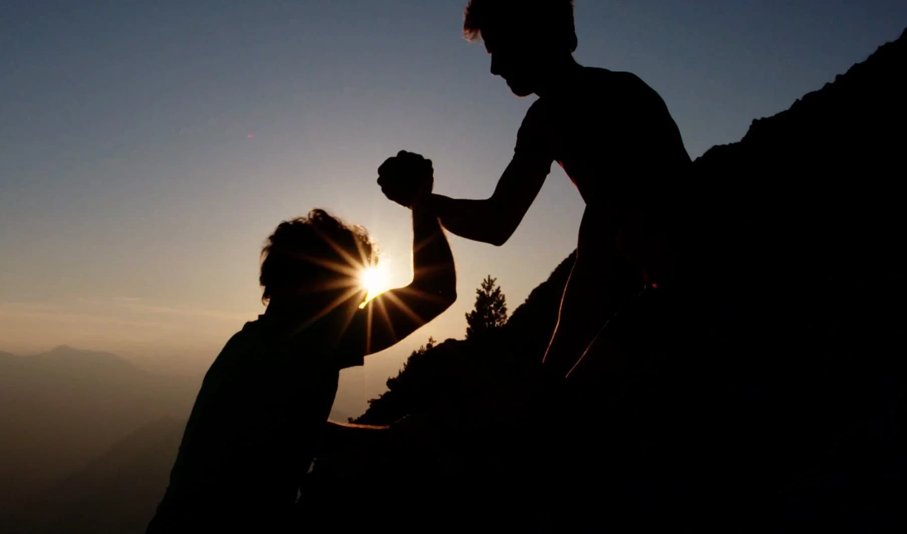 A helping hand reaching down to lift someone up a mountain trail at sunset